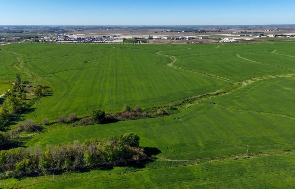 Aerial view of Iowa's agricultural landscape with green fields and industrial facilities in the distance.