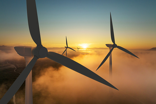 Wind turbines silhouetted against a golden sunrise.