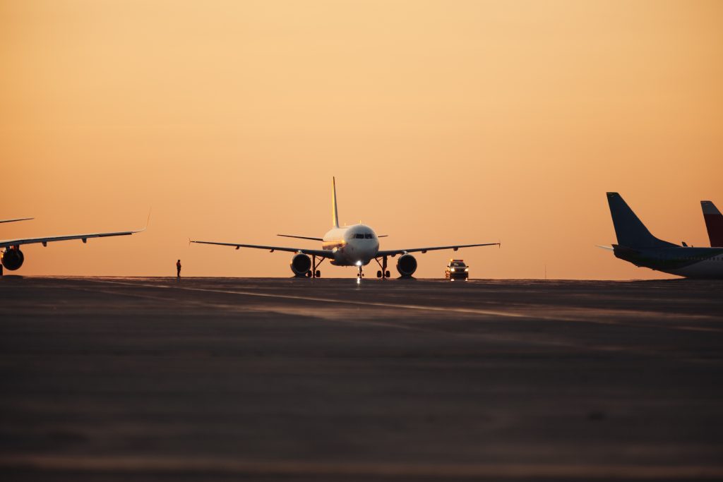 Commercial aircraft parked on airport tarmac at sunset.
