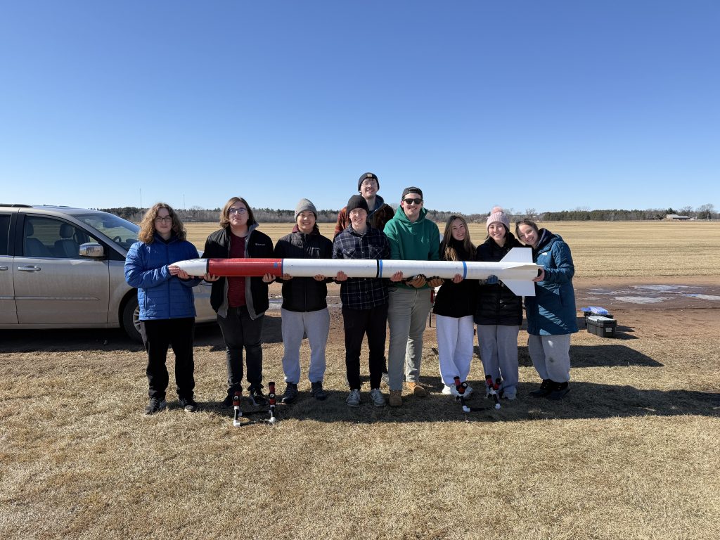 Students standing in a field holding a rocket